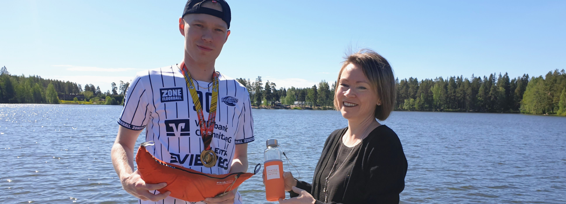 Kuvassa kunnanjohtaja ja Niki Lemberg veden äärellä, kädessään riippumatto ja vesipullo.